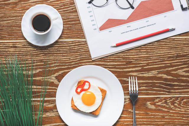 a coffee, fork, a plate with an egg papers and glasses on the table