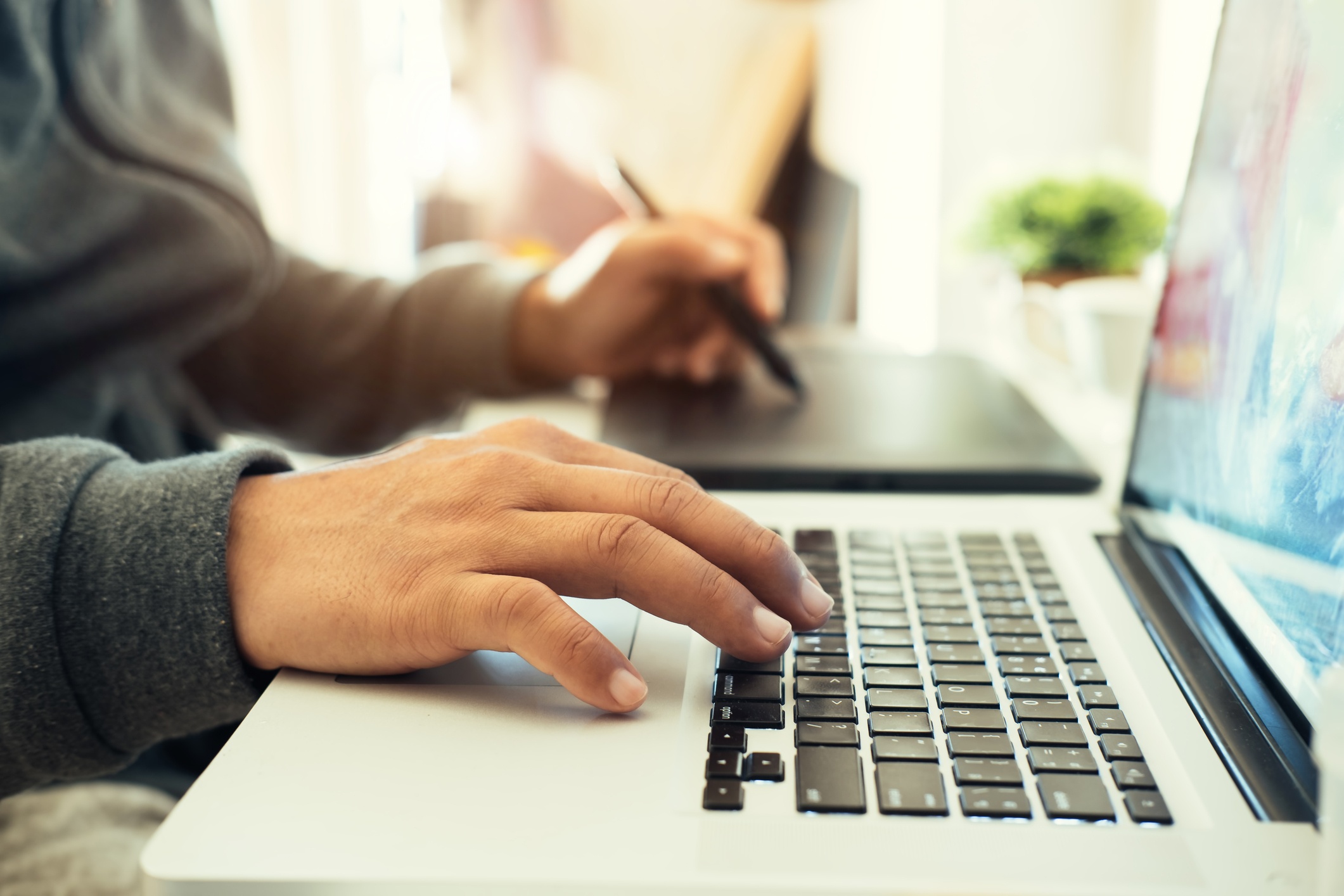 A hand writing and at the same time typing on a laptop