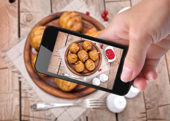 A hand with a phone taking picture of the food on the table