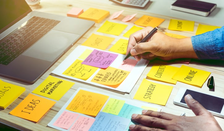 Content strategist writing notes on sticky note pads with laptop in front