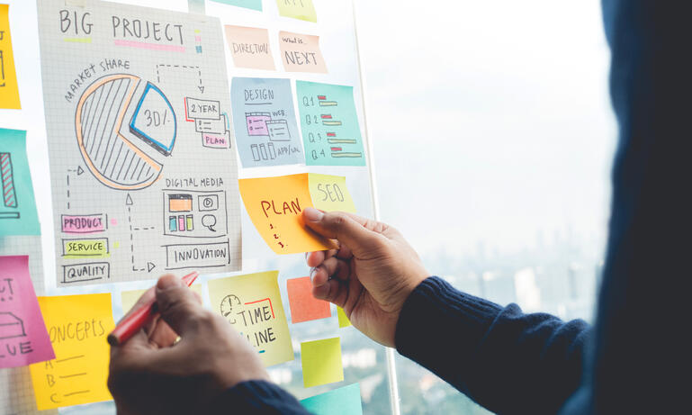  A man putting a sticky note with plans on the whiteboard while holding a pen.