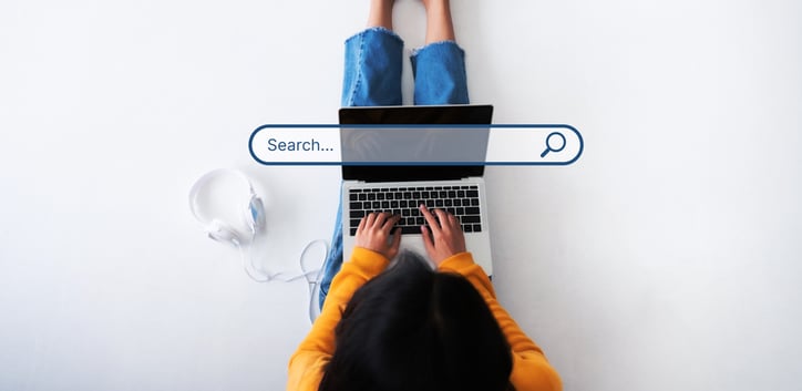 woman sitting on white floor with laptop on lap and earphones to the left side on the ground. Overlay "search" bar on picture signifying that the woman is doing a search on a browser.