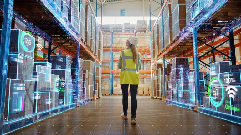 A woman standing in the middle of stock room looking up at the pile of boxes.