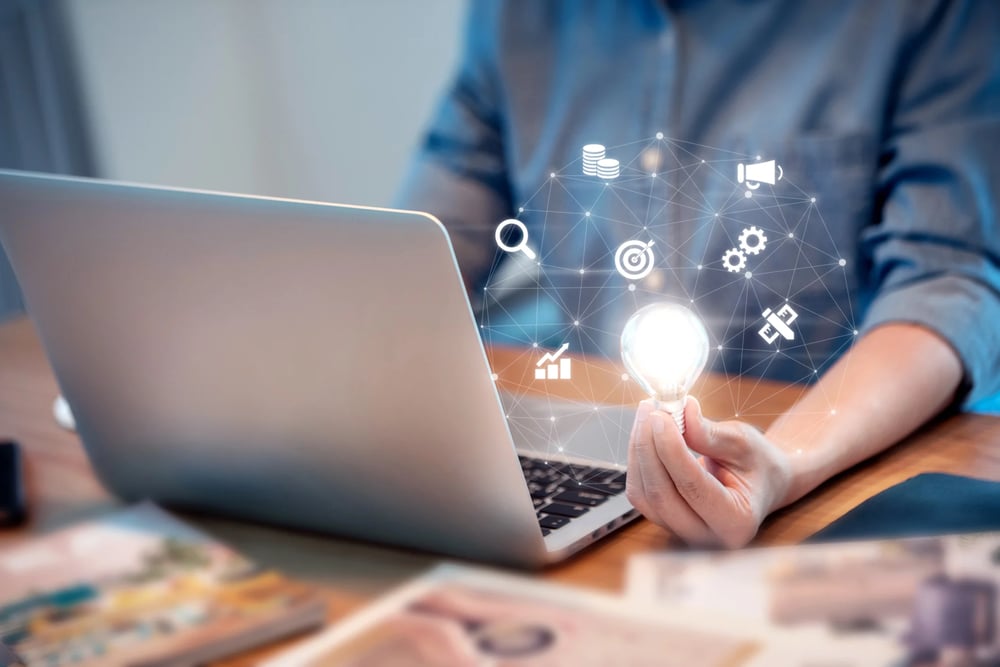 A man holding a bulb in front of a laptop.