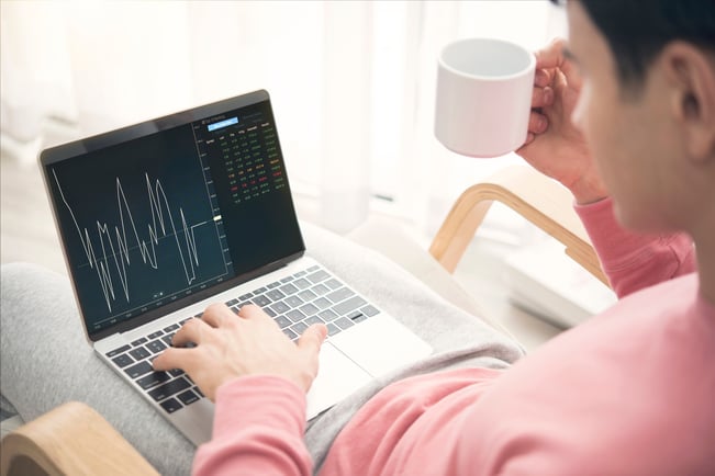 A man holding a cup of coffee on the right hand is working on a graph on his laptop