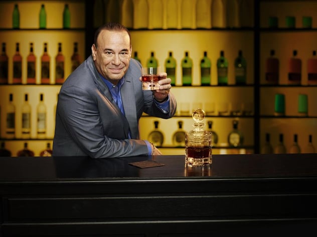 Jon Taffer holding a glass of wine inside a bar full of bottled wines