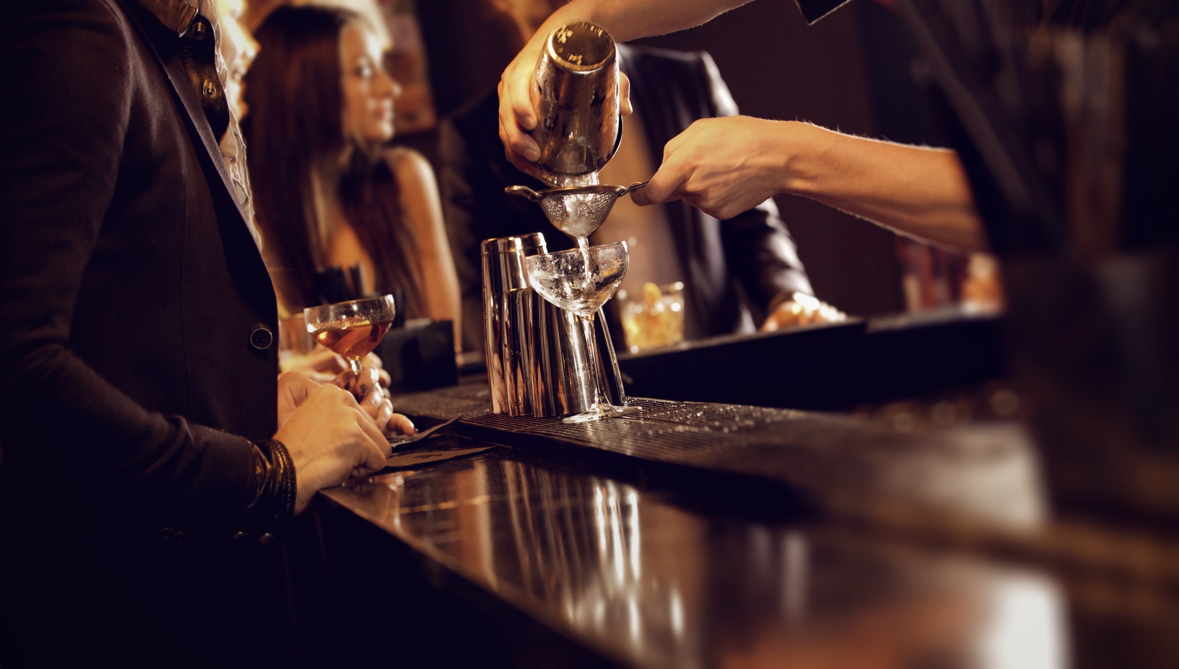 A bartender pouring the drink on the lady's glass