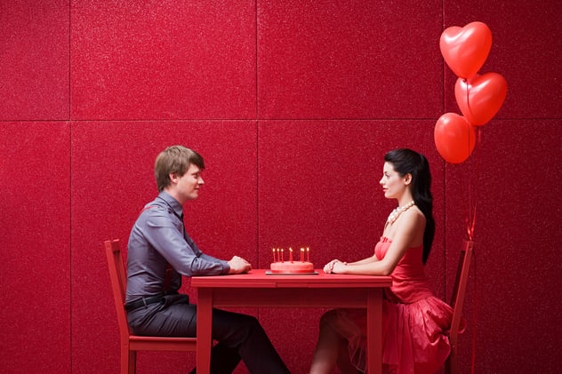 A man and  a woman facing each other on a dining table with  a cake.