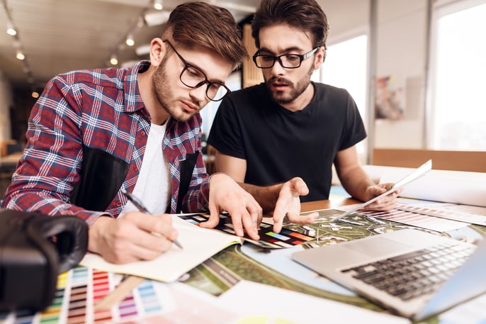 Two men wearing eyeglasses working on design in front of a laptop