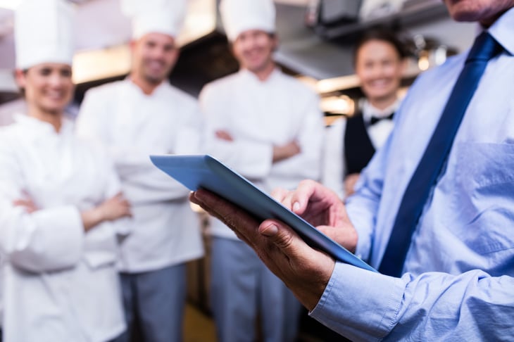 A manager having a meeting with his kitchen staff while holding his tablet