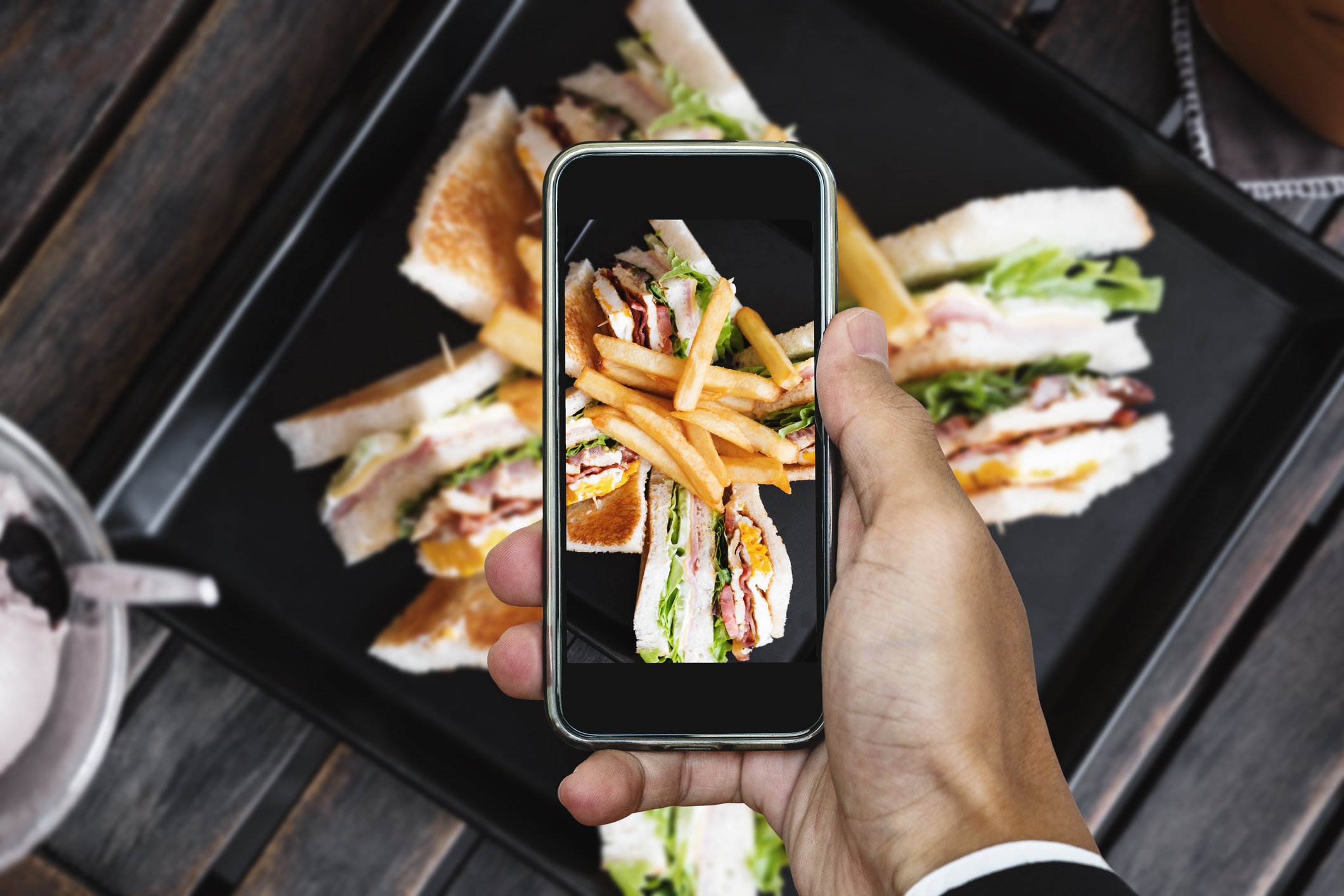 Capturing a sandwich with fries on a cellphone. 