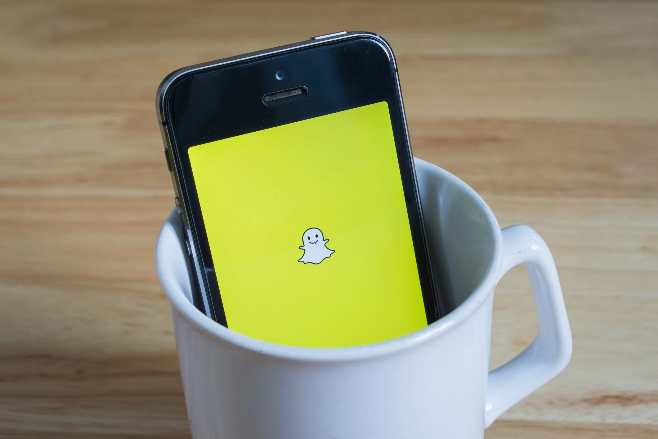 A phone inside a white cup with snapchat icon on screen